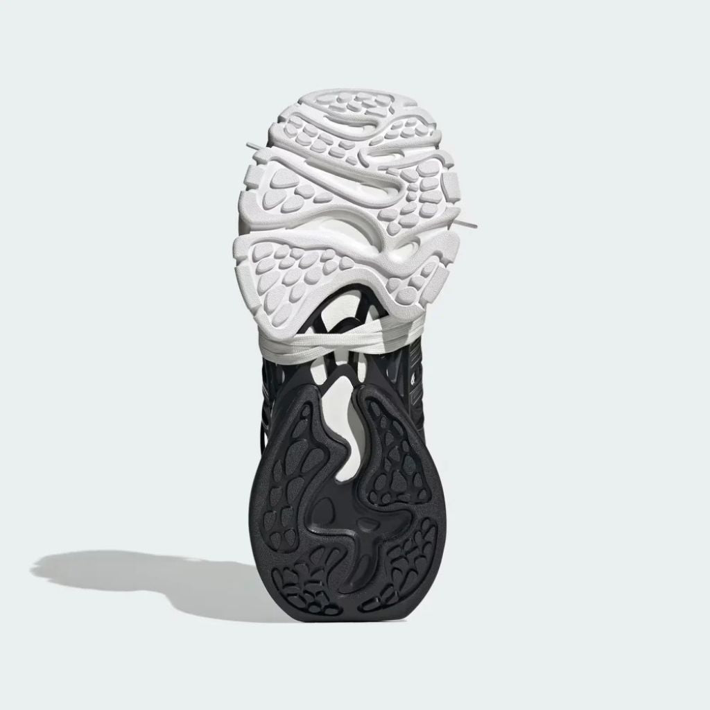 Sneaker Adidas XLG Runner Deluxe in bianco e nero con design ispirato agli anni 200, tomaia stratificata in tessuto e pelle, e suola spessa in gomma.