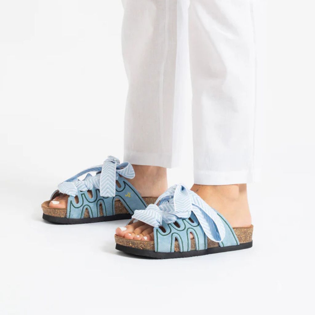 Ciabatta in camoscio celeste Jammers London con ricami verdi e grande laccio azzurro annodato.