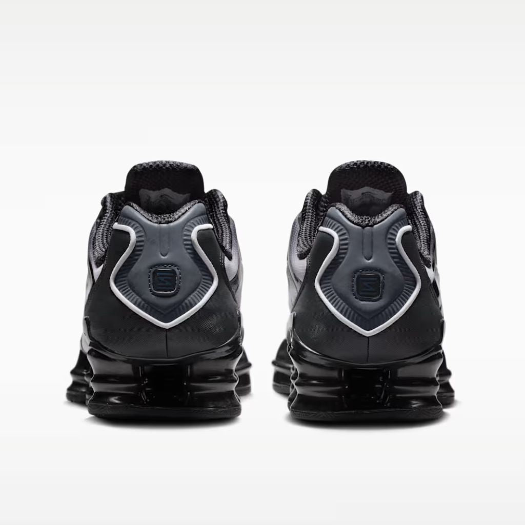 Sneaker Nike Shox TL con tomaia sfumata dal nero all'Off Noir, gabbia esterna sagomata e suola con colonne ammortizzanti integrali su fondo bianco.