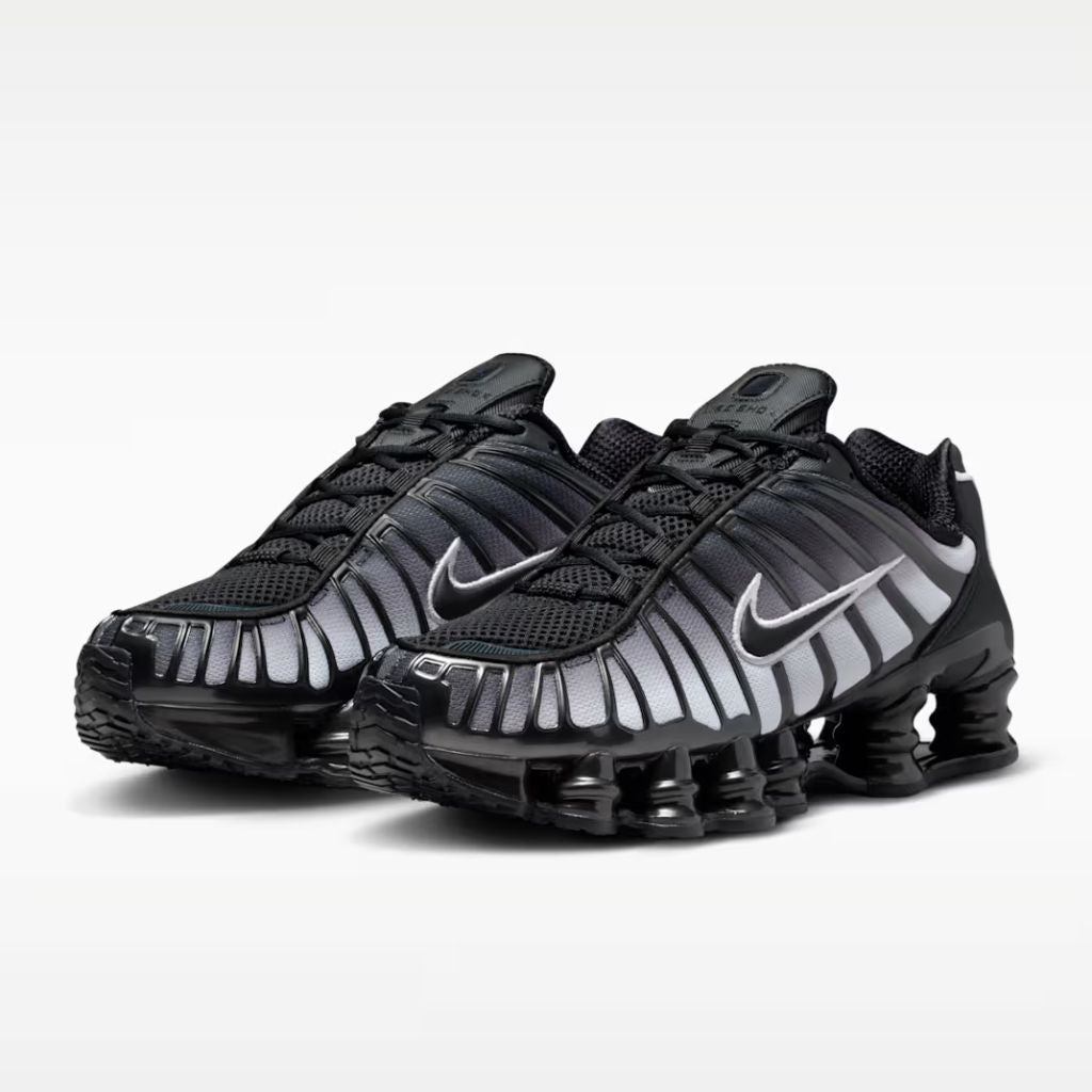 Sneaker Nike Shox TL con tomaia sfumata dal nero all'Off Noir, gabbia esterna sagomata e suola con colonne ammortizzanti integrali su fondo bianco.