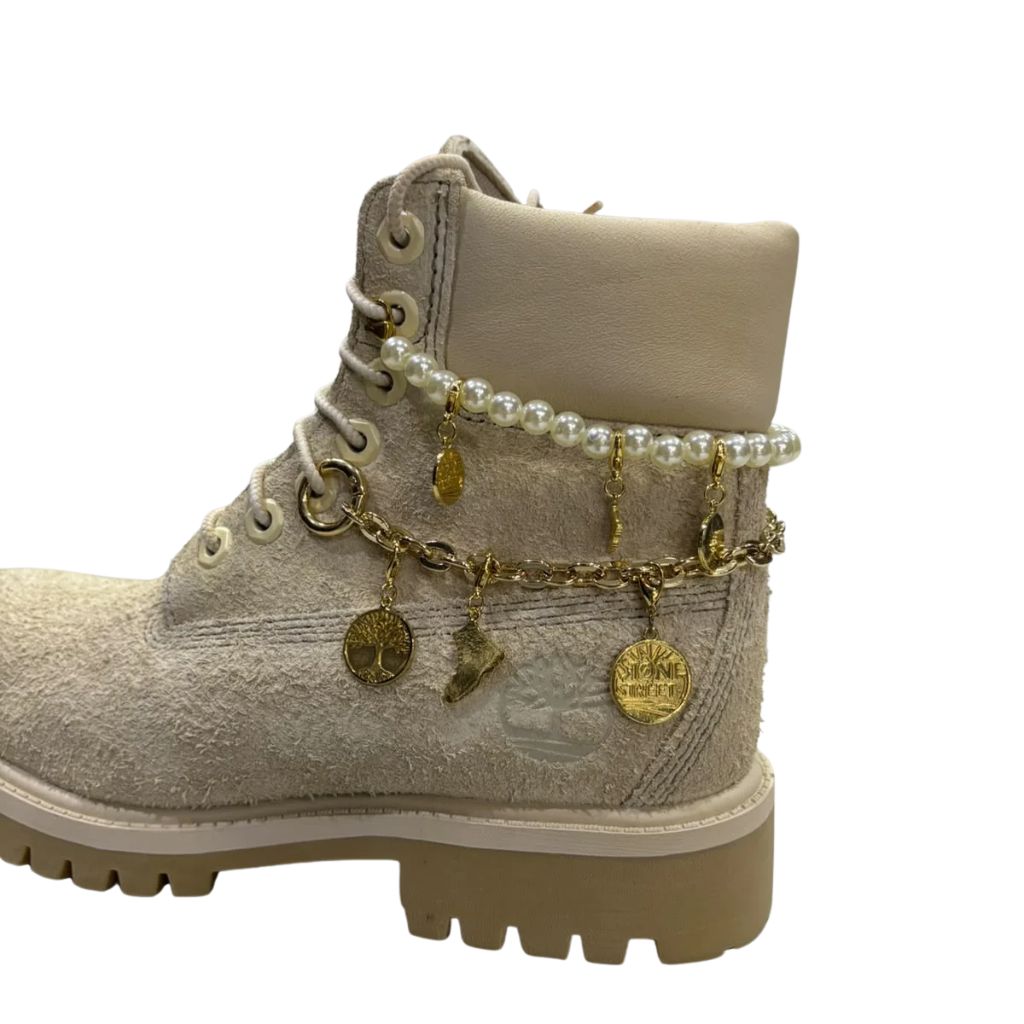 Stivaletto stringato Timberland Heritage 6-Inch in nabuk scamosciato beige chiaro con filo di perle, catena dorata e ciondoli pendenti.