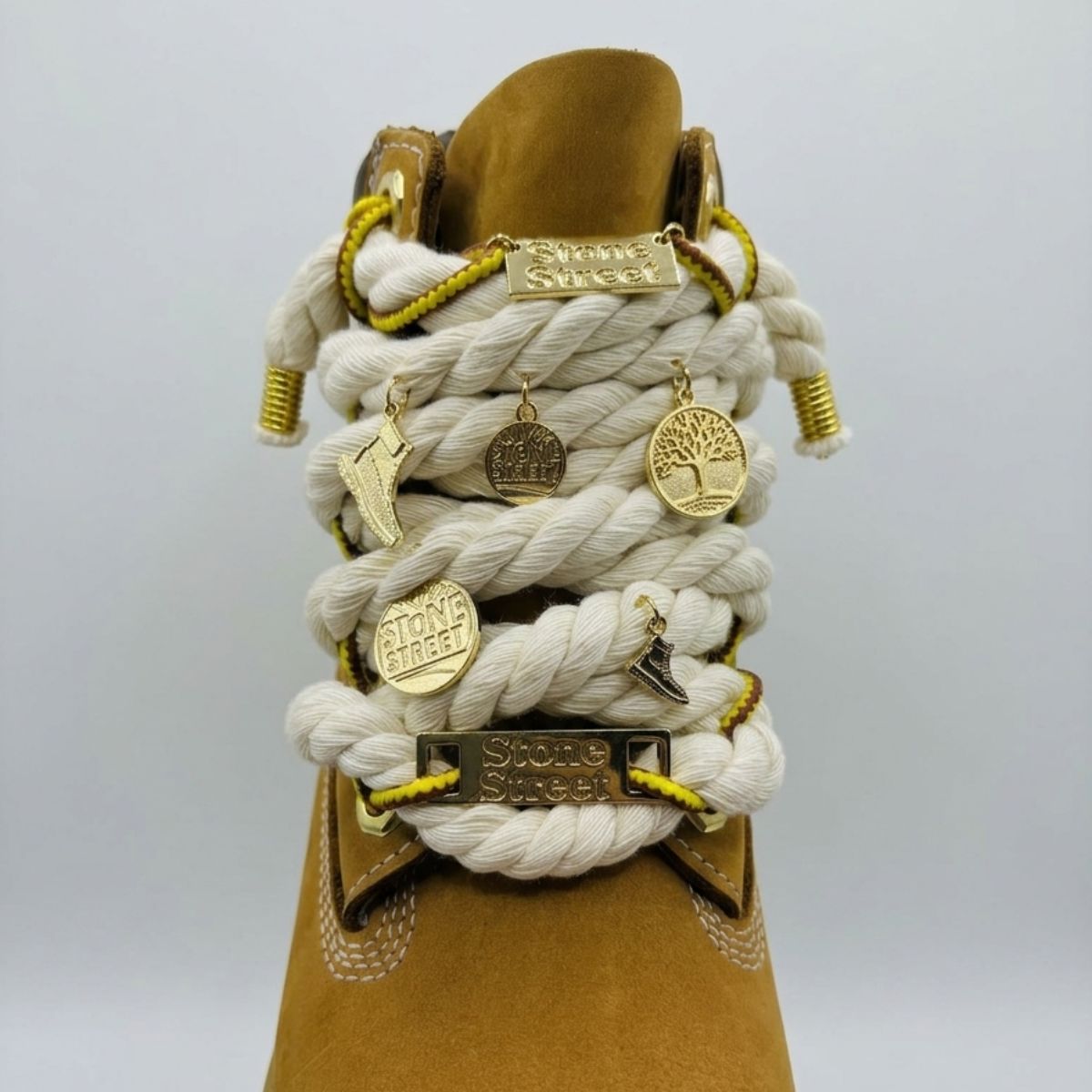 Stivale robusto in nabuk color giallo ocra, con allacciatura artistica a corda beige spessa decorata con charm placcati in oro.