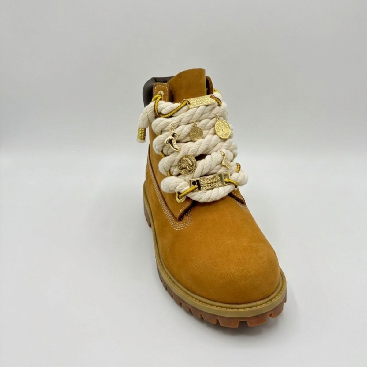 Stivale robusto in nabuk color giallo ocra, con allacciatura artistica a corda beige spessa decorata con charm placcati in oro.
