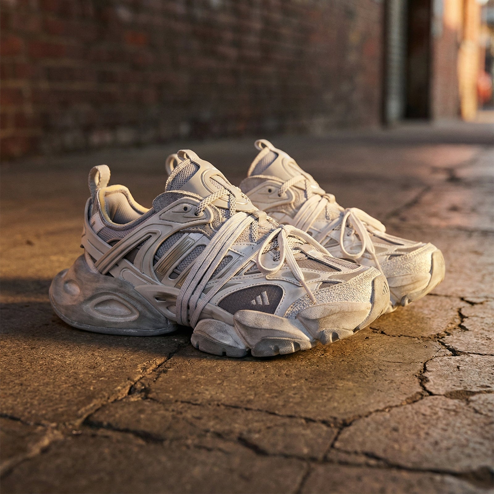 Adidas XLG Runner Deluxe sneakers beige e grigie su pavimentazione in pietra, street style urban, luce del tramonto