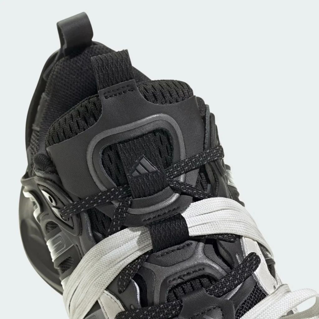 Sneaker Adidas XLG Runner Deluxe in bianco e nero con design ispirato agli anni 200, tomaia stratificata in tessuto e pelle, e suola spessa in gomma.