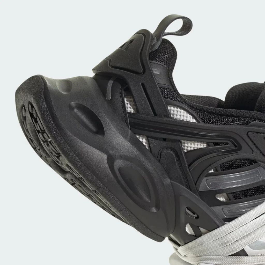 Sneaker Adidas XLG Runner Deluxe in bianco e nero con design ispirato agli anni 200, tomaia stratificata in tessuto e pelle, e suola spessa in gomma.