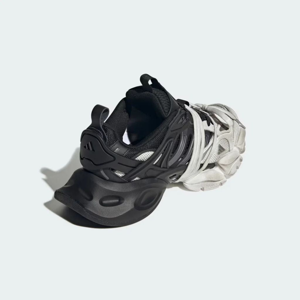 Sneaker Adidas XLG Runner Deluxe in bianco e nero con design ispirato agli anni 200, tomaia stratificata in tessuto e pelle, e suola spessa in gomma.