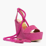 Sandalo con zeppa alta 11 cm in camoscio fucsia e lacci a corda intrecciati alla caviglia.
