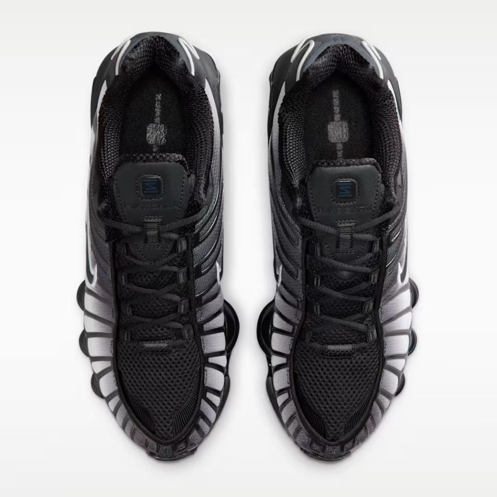 Sneaker Nike Shox TL con tomaia sfumata dal nero all'Off Noir, gabbia esterna sagomata e suola con colonne ammortizzanti integrali su fondo bianco.