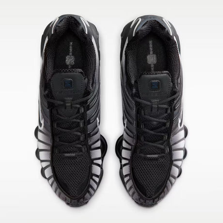 Sneaker Nike Shox TL con tomaia sfumata dal nero all'Off Noir, gabbia esterna sagomata e suola con colonne ammortizzanti integrali su fondo bianco.