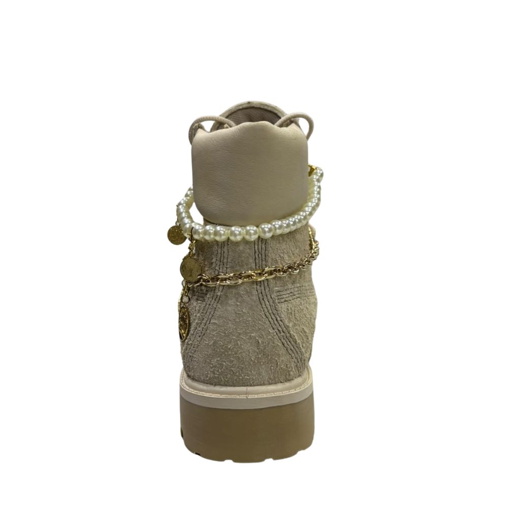 Stivaletto stringato Timberland Heritage 6-Inch in nabuk scamosciato beige chiaro con filo di perle, catena dorata e ciondoli pendenti.