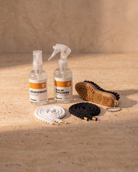 Lacci di corda bianchi e neri con puntali oro e kit di cura Timberland su travertino